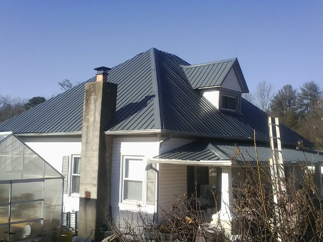 Dark blue standing seam metal roof on a white farmhouse with dormer — Slate & Tile Roof Repair by Roofing Brothers in Dilliner