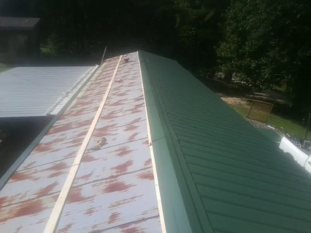 Old rusted panels beside newly installed green metal roofing — Wind Damage Roof Repair by Roofing Brothers in Dilliner