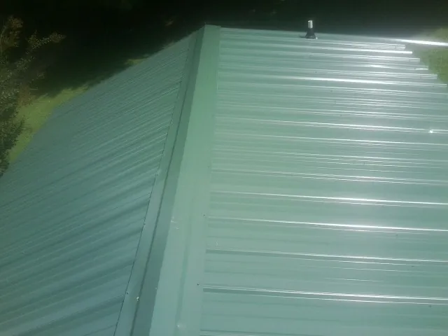 New green metal panels meeting at the ridge of a roof — Flat Roof Repair work by our crew in Dilliner