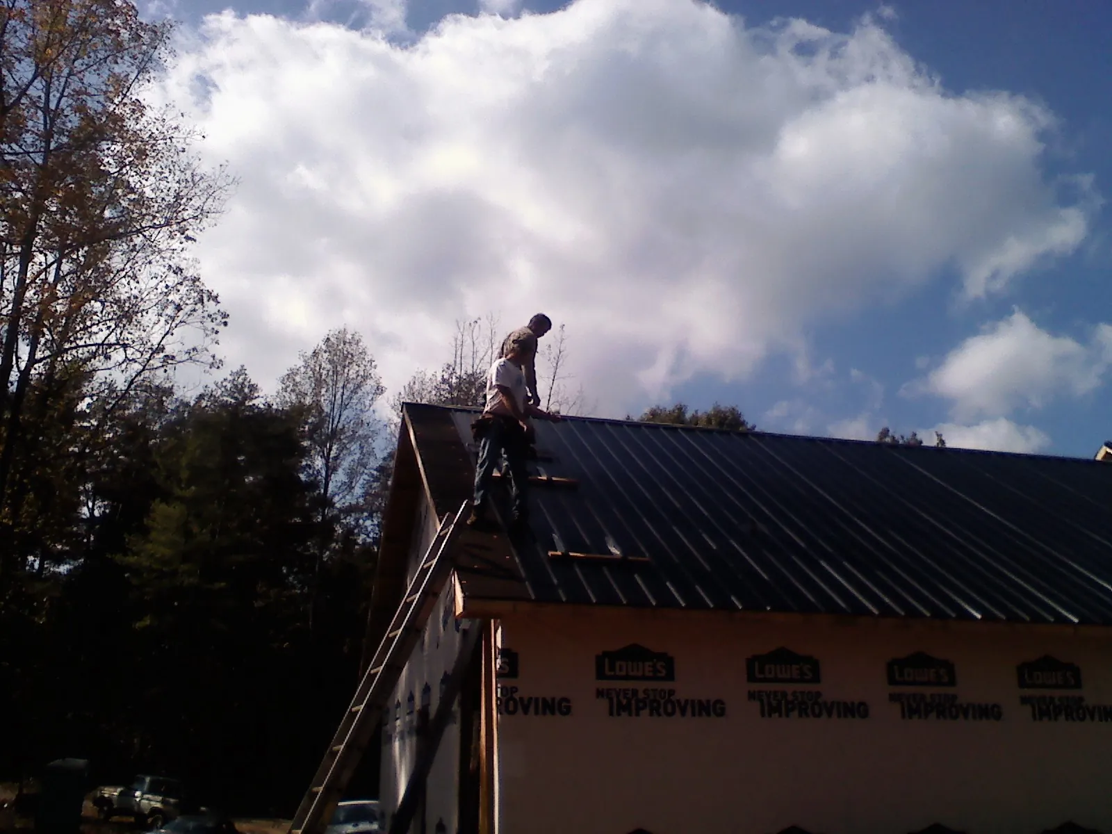 Roofer fastening dark metal panels high against a cloudy sky, from a Roof Inspection job in Dilliner