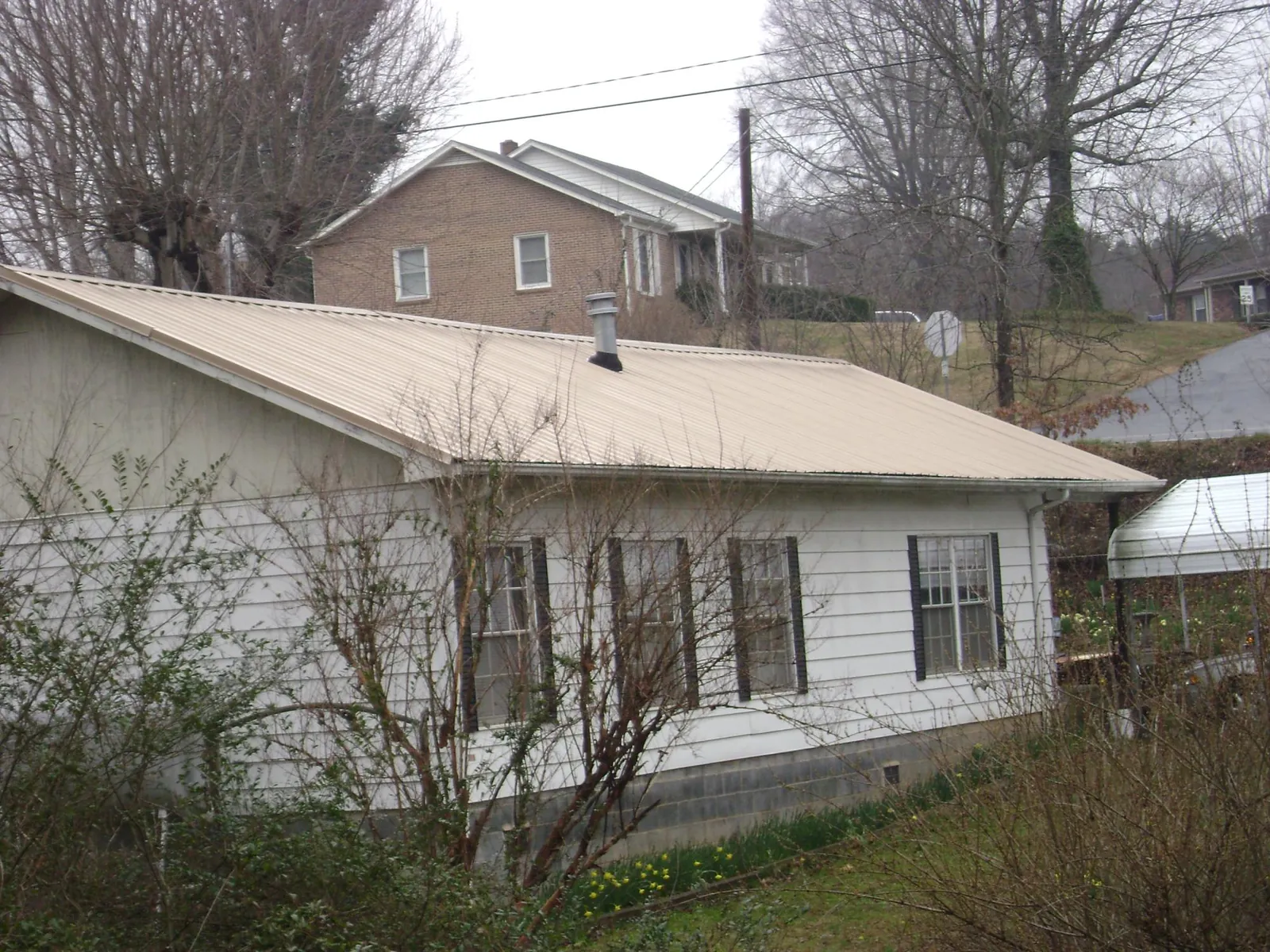 Tan metal roof on a white sided house set into a hillside — Commercial Roofing by Roofing Brothers in Dilliner