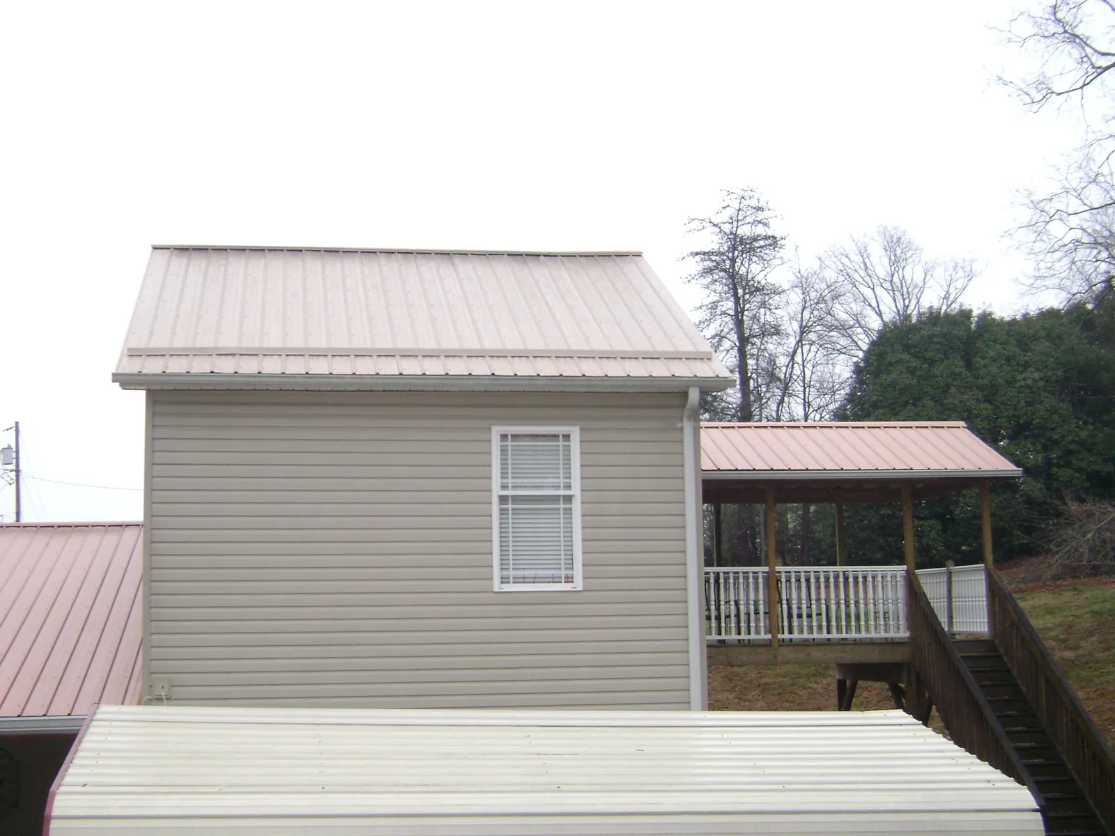 Tan metal roofs on a two story addition and attached porch, from a Roof Replacement job in Dilliner